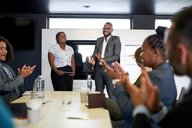 Group of mixed race colleagues in modern meeting room with laptop computer encouraging two attractive African American business professionals leading a collaborative discussion